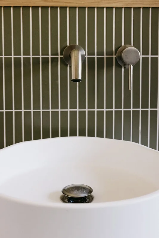 Wall-mounted tap and basin against green tiles